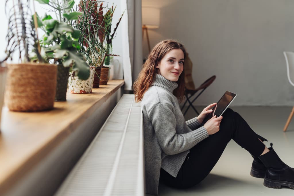 Vrouw zit met iPad tegen radiator aan
