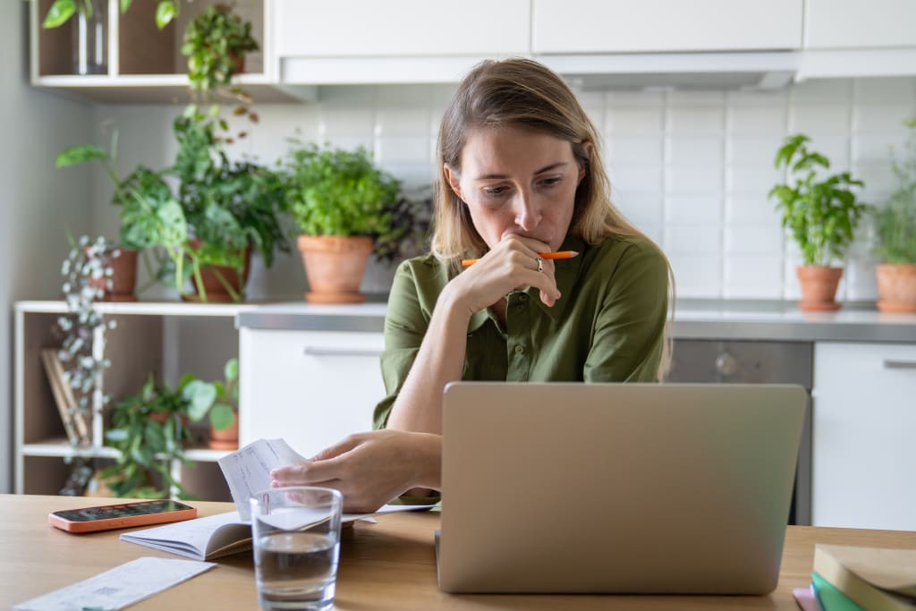 Vrouw kijkt bezorgd naar haar laptop aan de keukentafel