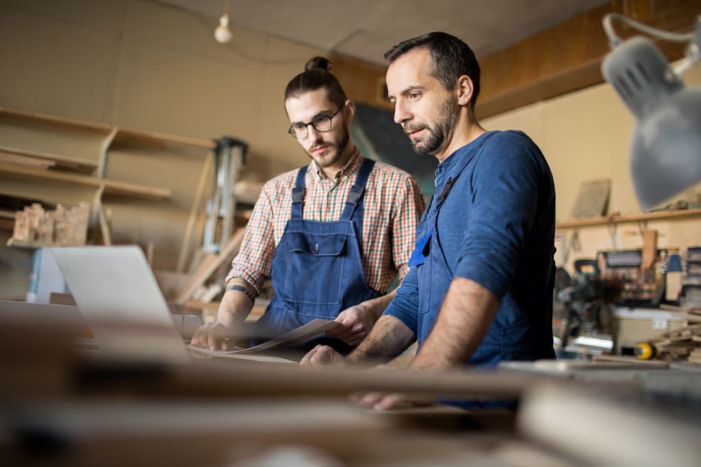 Vakspecialist en bewoner samen achter een laptop in werkplaats
