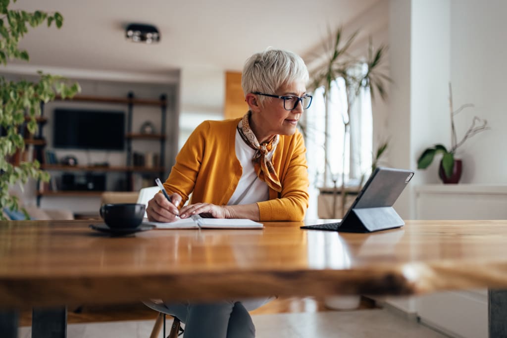 Vrouw zit aan keukentafel met ipad en notitieblok