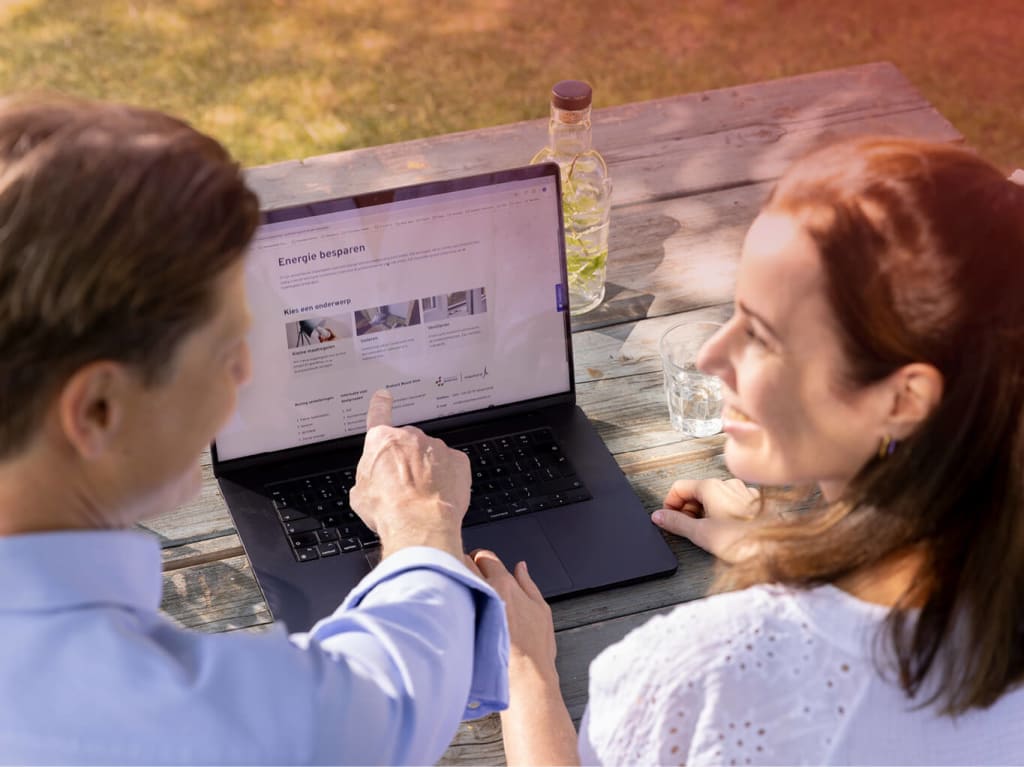 Meneer en mevrouw lachen naar elkaar en wijzen naar een laptop