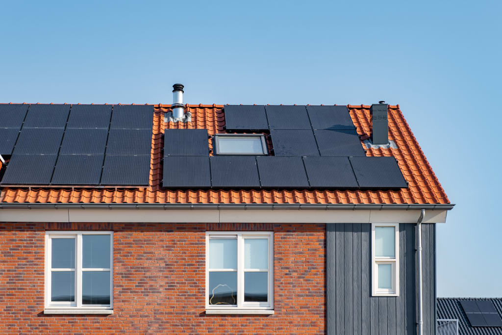 Een hoekwoning met zwarte zonnepanelen op een oranje dak.