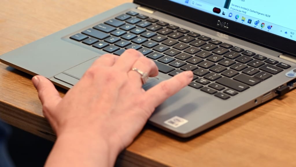 Een toetsenbord van een werklaptop met een hand die bij de touchpad zit.