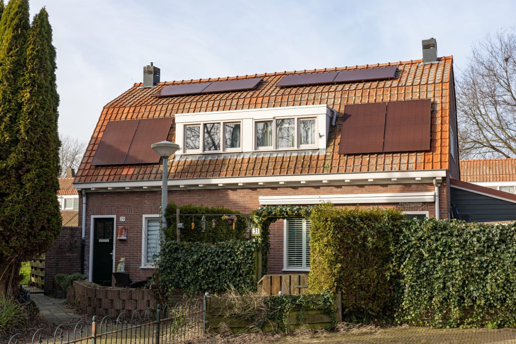 Een vrijstaande woning met zonnepanelen en een heg voor de tuin.