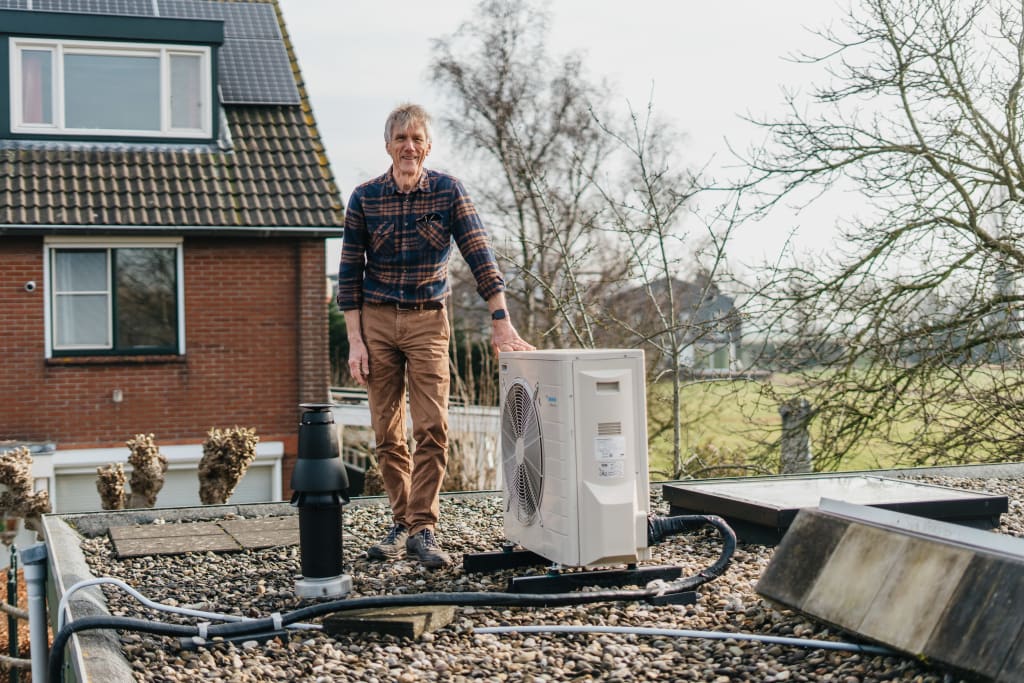 Een foto van een witte man die op een plat dak staat, hij staat naast zijn hybride warmtepomp