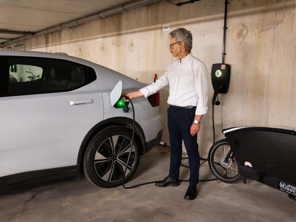 Een man die een elektrische auto aan het opladen is in een parkeergarage, terwijl de laadpaal in de achtergrond zichtbaar is.