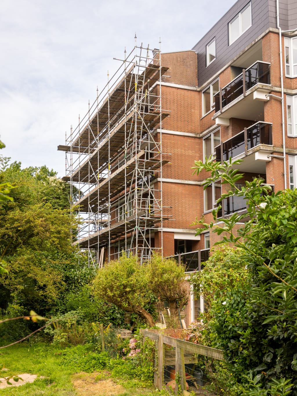 Een gebouw met een steiger rondom het gedeelte dat wordt gerenoveerd, met groen in de omgeving.