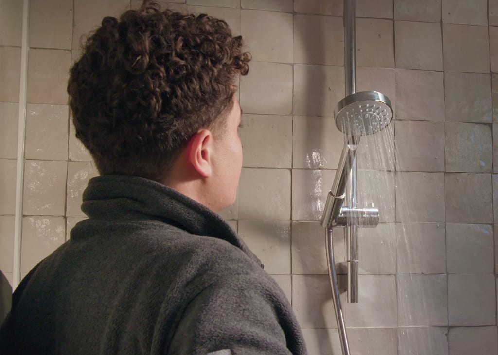 Een persoon in een badjas kijkt naar stromend water uit een douchekop