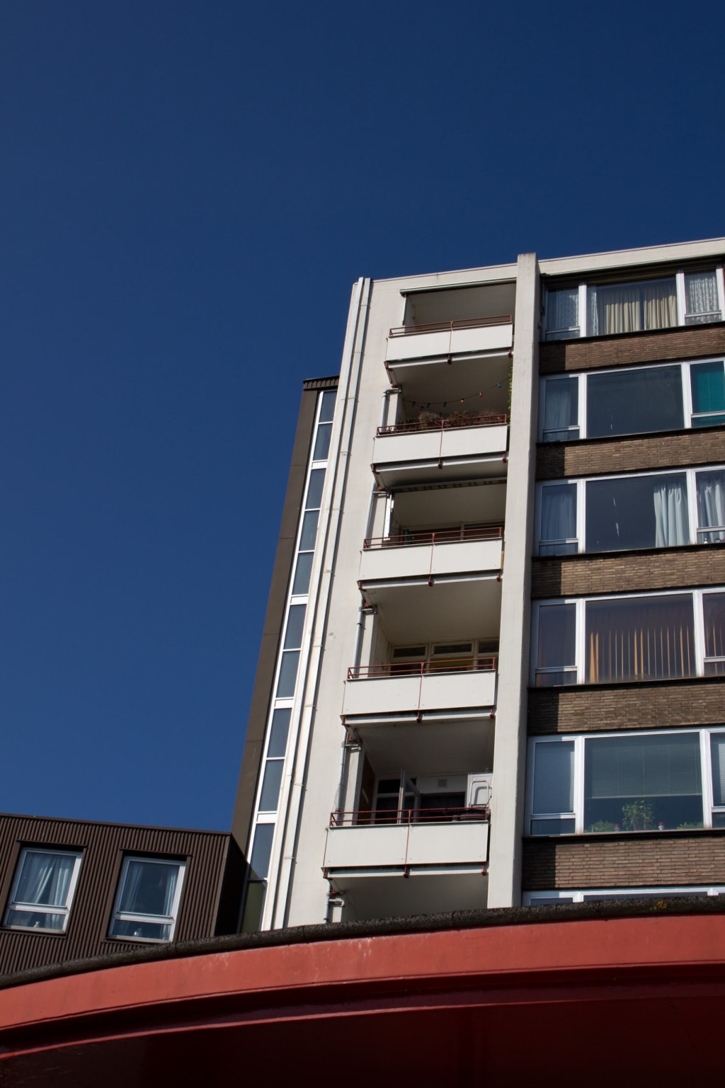 Een flatgebouw met meerdere verdiepingen en balkons, gefotografeerd vanaf de grond tegen een blauwe lucht.