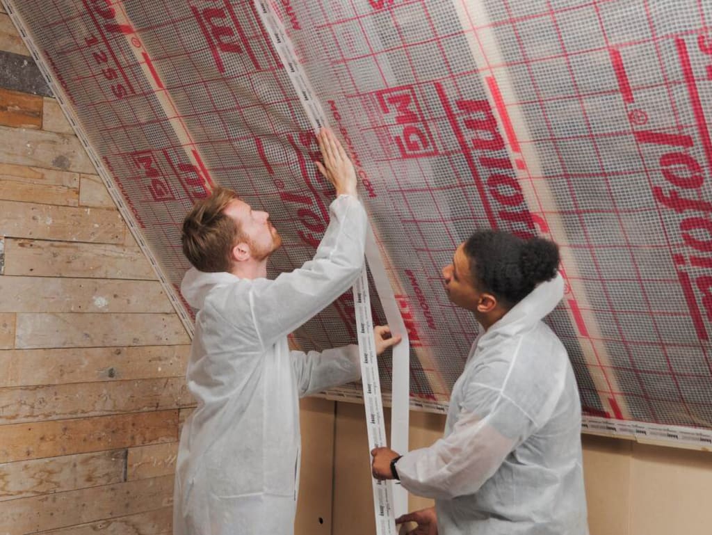 Twee mensen in witte overalls brengen isolatiefolie aan tegen een schuin dak