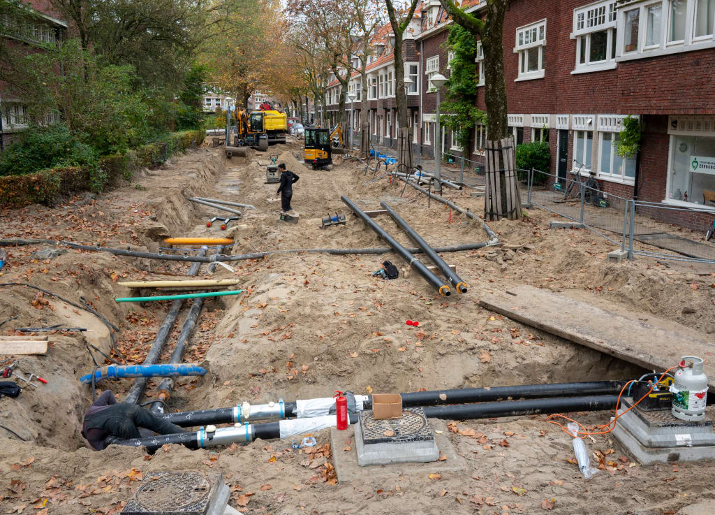 Arbeiders zijn bezig met het installeren van leidingen in een open gegraven straat.
