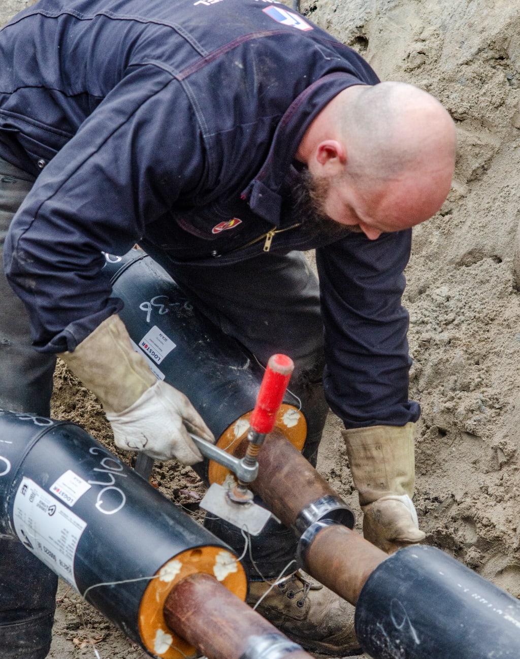 Een man werkt in een kuil aan het aansluiten van pijpen met behulp van gereedschap.
