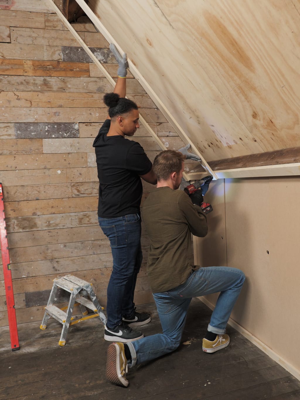 Twee mensen werken samen om een houten plaat aan een muur te bevestigen met een schroevendraaier in een ruimte met een houten achtergrond.
