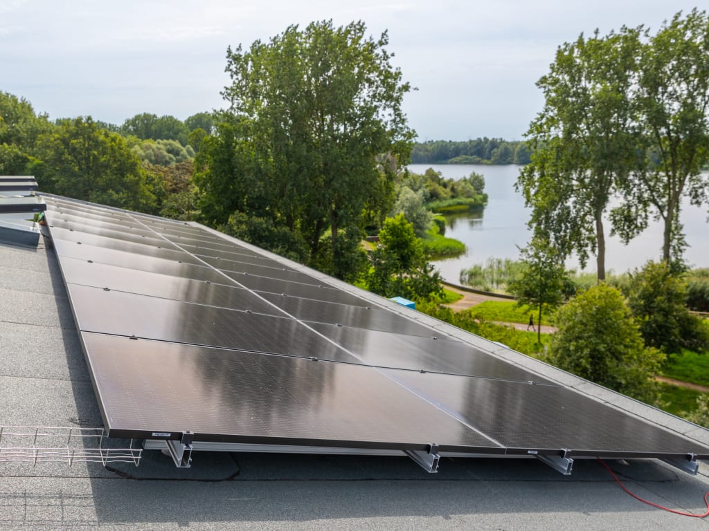 Zonnepanelen op een plat dak aan de rand van een natuurgebied met zicht op een meer.
