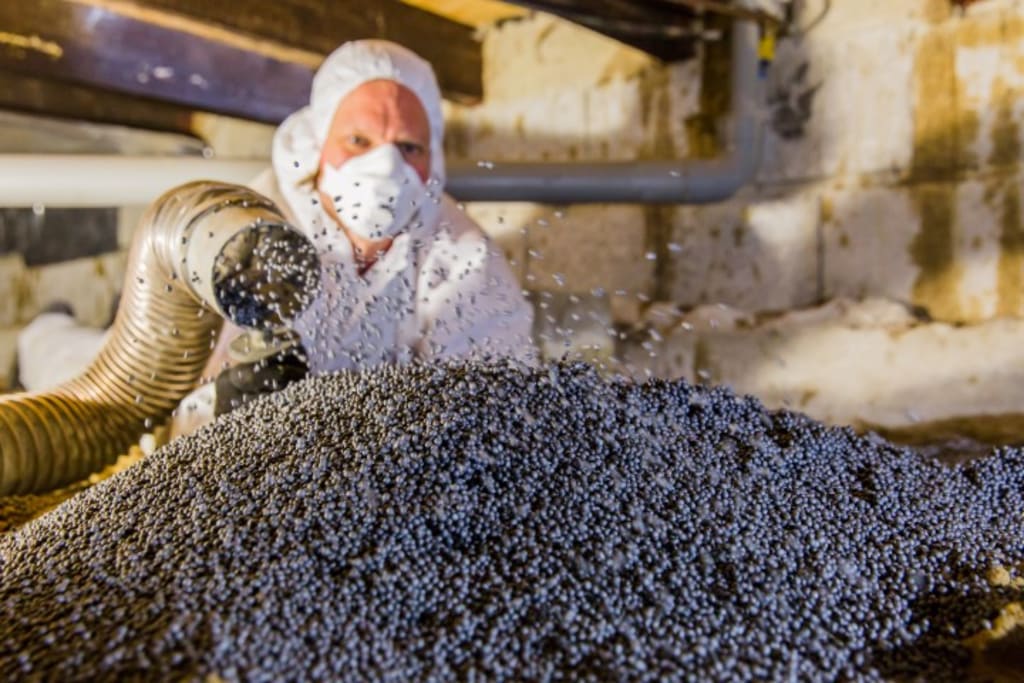 Iemand in een wit pak die EPS parels ter bodemisolatie in een kruipruimte spuit met een buis.