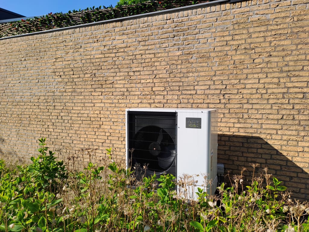 Buitenunit warmtepomp voor een stenen muur naast de woning geplaatst