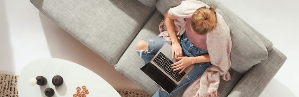 Foto van een mevrouw achter haar laptop en zittend op de bank.