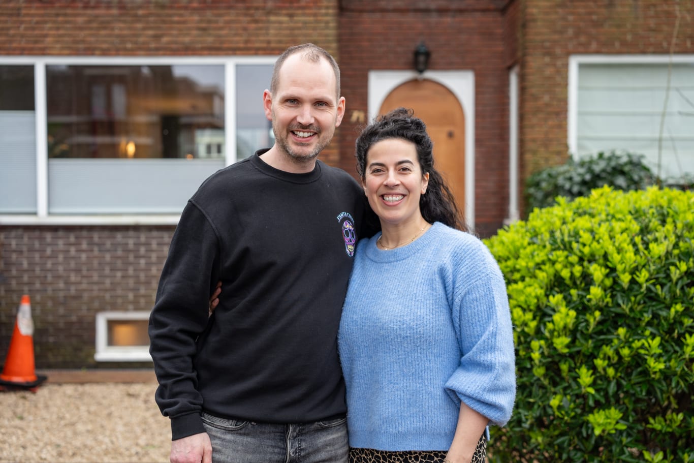 Een man en vrouw staan arm in arm voor hun huis