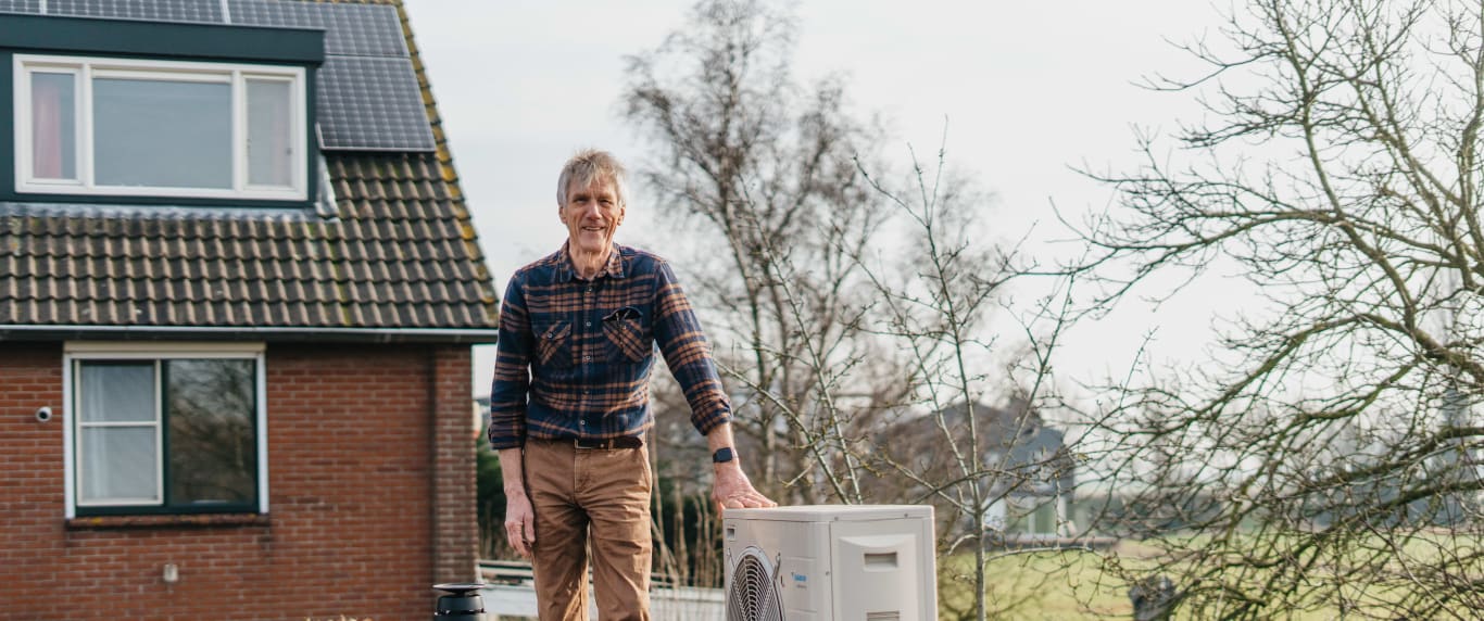 Een foto van een witte man die op een plat dak staat, hij staat naast zijn hybride warmtepomp