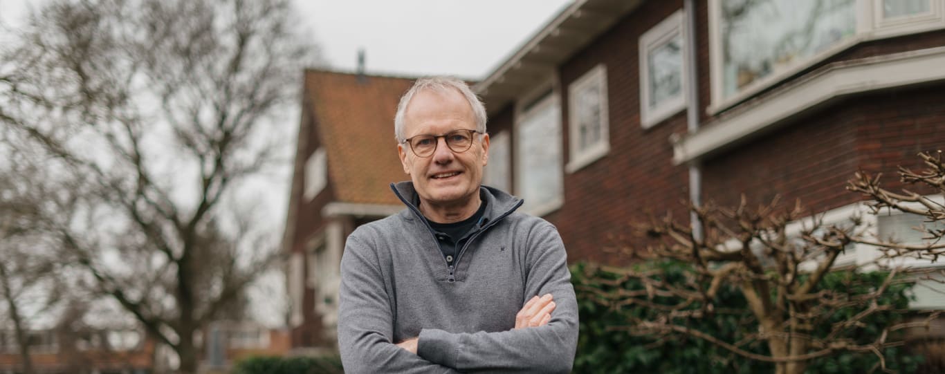 Tom Swart uit Amstelveen. Een witte man met zijn handen over elkaar gekruist, hij staat in een straat met huizen achter zich.