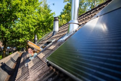 Mevrouw hangt uit haar dakraam en kijkt naar de zonnepaneel op haar dak.