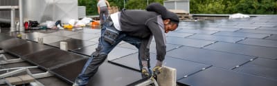 Foto van een man die zonnepanelen installeert op een plat dak.