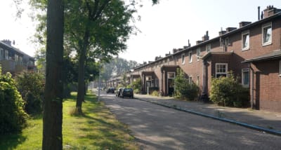 Rijtjeshuizen van baksteen langs een rustige straat met bomen en geparkeerde auto's.