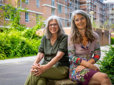 Twee vrouwen poseren zittend voor gebouwen