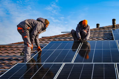 Twee vakspecialisten zijn zonnepanelen aan het installeren op een dak.