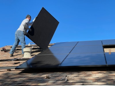 Een man is zonnepanelen aan het leggen op een schuin dak