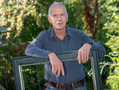 Foto van Peter die op een frame van een raam leunt.