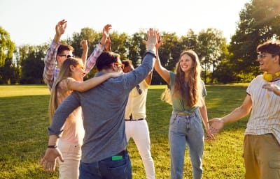 Groep jonge mensen in de avondzon op grasveld die blij zijn en elkaar high five geven.