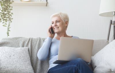 Mevrouw houdt haar laptop vast en praat aan de telefoon.