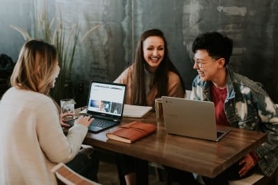 drie lachende mensen rondom een tafel met laptops