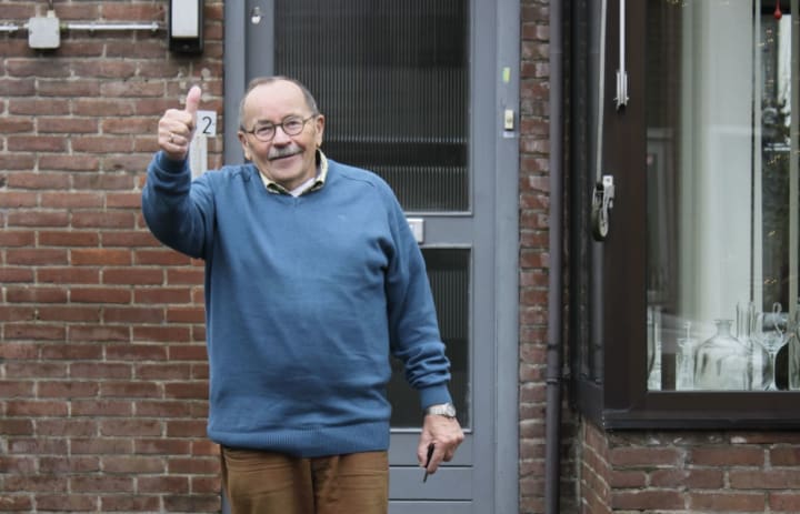 Meneer staat op de foto voor zijn voordeur en steekt zijn duim omhoog