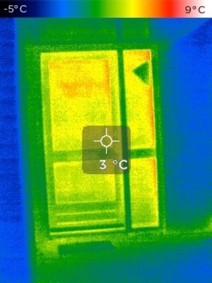 Een infraroodscan van een raam in een woning. De afbeelding is voornamelijk geel, groen en blauw.