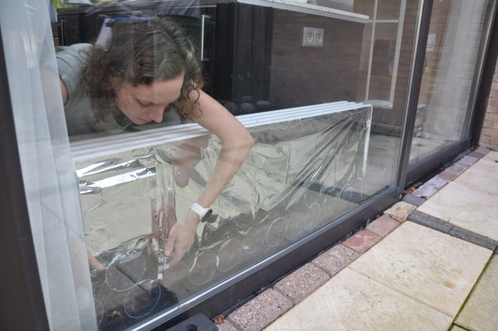 Radiatorfolie wordt geplaatst achter op een verwarming die voor een raam staat