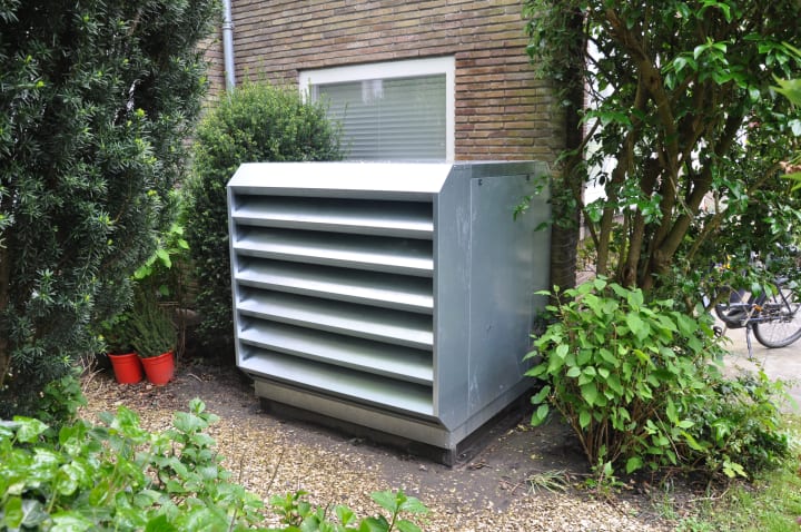 Geluiddempende kast rondom warmtepomp naast een woonhuis met groen ernaast