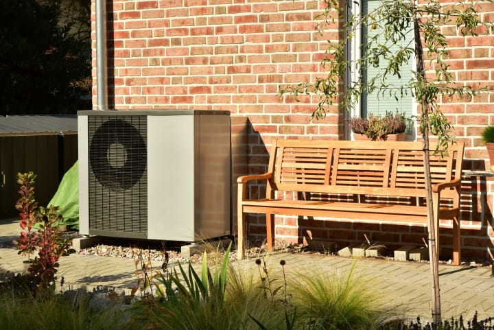 Warmtepomp naast bankje in de zon in een tuin