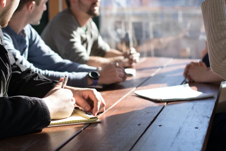 Foto van een groep mensen aan tafel met notitieblokken